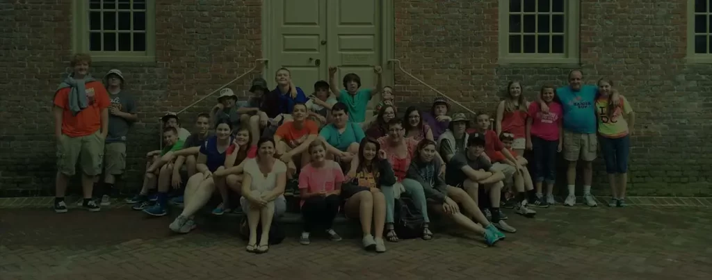 A tour group sitting on the steps of a building against a door